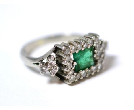 An emerald and diamond cluster ring, a step cut emerald within a border of eight-cut diamonds, a trio of further diamonds to 