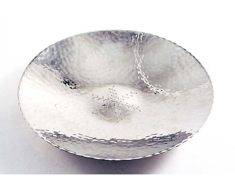 A 20TH CENTURY STAINLESS STEEL DISH with a hammered finish and a chased design in the centre, by the Keswick School of Indust