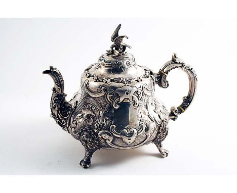 A VICTORIAN ORNATE TEA POT on four grotesque mask & paw feet with an embossed body, a domed cover and bird finial, each side 