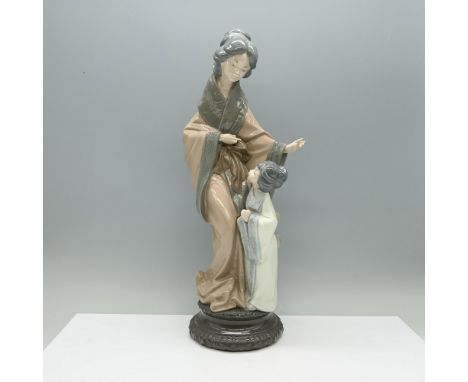 A figurine of a nurturing mother in a brown and green robe, her open hand extending warmth and protection, while her child, d