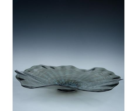 A light, unique clear sculpture in a form of a footed bowl with a scalloped rim, and black and gray swirls. The piece can be 