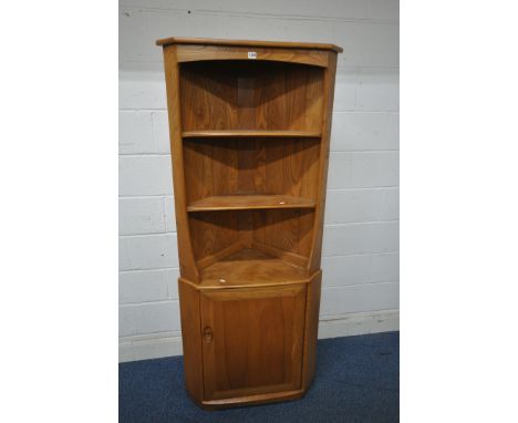 AN ERCOL ELM CORNER CUPBOARD, with two shelves, above a single cupboard door enclosing another shelf, width 76cm x depth 44cm