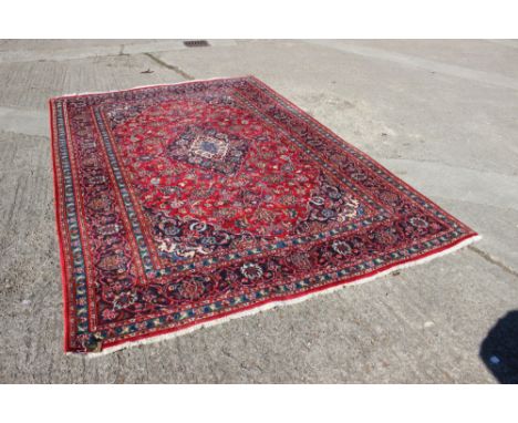 A Kirman rug with blue and white floral central medallion on a red figured ground, 114" x 79" approx