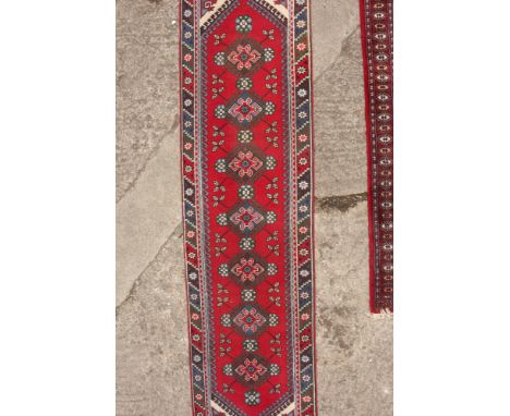 A Kazak runner with seven tarantula guls on a red ground, 114" x 30" approx