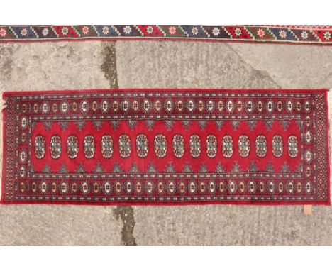 A Bokhara runner with sixteen guls on a red ground, 75" x 26" approx