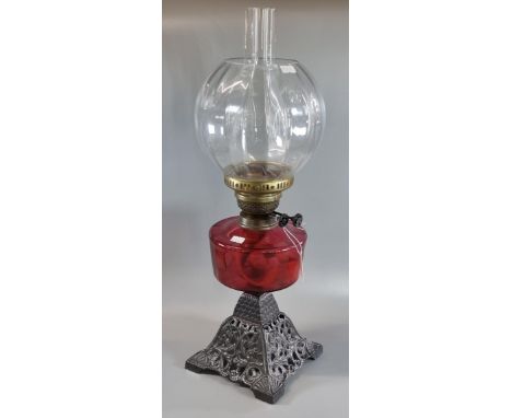 Early 20th century double oil burner lamp having glass globular shade above a cranberry glass reservoir on a cast metal pierc