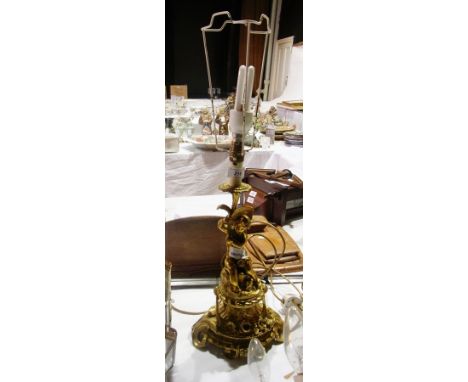 A decorative brass lamp with a cherub holding the light, on a stem, floral scroll base 