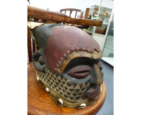 AN AFRICAN CARVED WOOD HEAD DRESS MASK WITH POLYCHROME DECORATION AND APPLIED HIDE AND COWREY SHELLS.