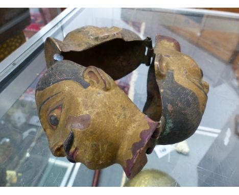AN EASTERN POLYCHROME DECORATED REPOUSSE COPPER MOUNT OF THREE MALE MASKS TOGETHER WITH A CARVED FOO LION NETSUKE.