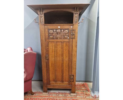 An Arts and Crafts oak wardrobe, the broad top board over a door with a copper inset with three flower heads in relief, the n