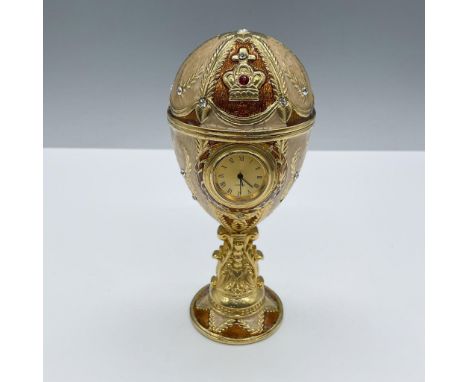 Bronze and beige enamel egg with gilt detailing and a quartz clock in the center. The egg opens to a blue satin interior. Dim