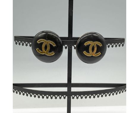 A pair of vintage Chanel clip-on earrings featuring the iconic interlocking CC logo in polished gold-tone metal against a bla