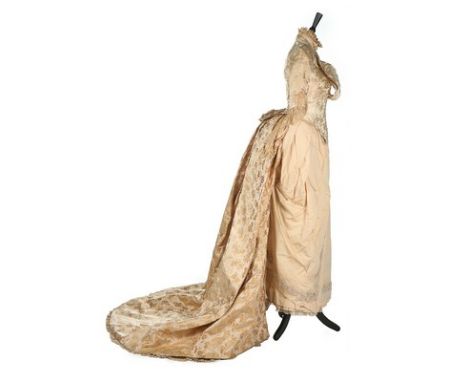 An ivory damask satin wedding dress, late 1880s, with corsetted bodice, the skirt with asymmetric pleats, integral bum-roll; 