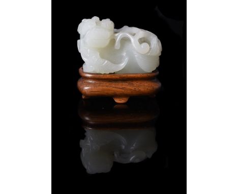 A Chinese pale celadon jade lion, Qing Dynasty, the lion carved seated and facing to the side, holding a large floral spray i