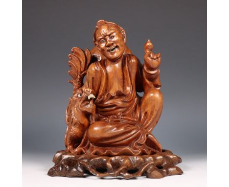 China, wooden sculpture of an Immortal, 20th century, in seated position and holding up a pearl for a dragon by his side, on 