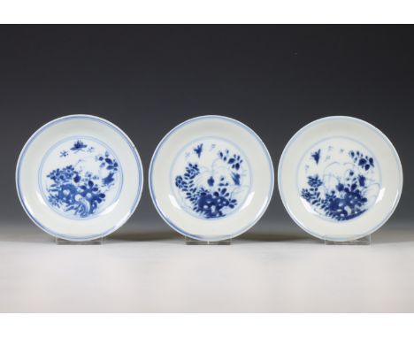 China, set of three blue and white saucers, early 18th century, each decorated with a butterfly in a flower garden, the base 