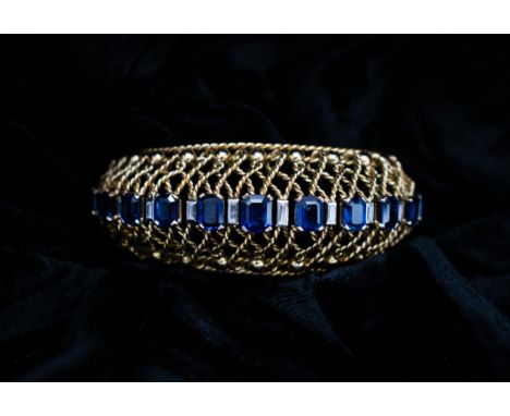 A Gubelin Sapphire and Diamond Bangle of graduated bombé form corner claw-set a row of graduated step-cut sapphires with rubo