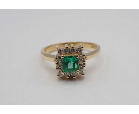 An Emerald and Diamond Cluster Ring corner claw-set step-cut emerald within a frame of fourteen brilliant-cut diamonds, stamp