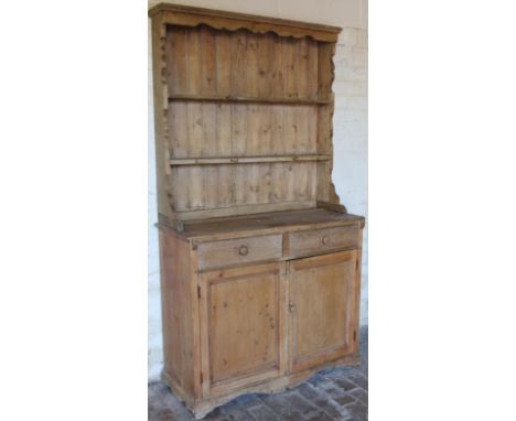 A stripped and lightly polished pine rustic kitchen dresser, the upper section with overhanging moulded top, raised above two