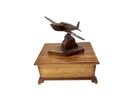 A box in the form of a humidor made of light lacquered wood. On the lid there is a pedestal with an airplane at the top. A mi