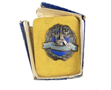 Badge in the form of a shield surrounded by a laurel wreath. Inside, on blue enamel, there is a visible monument of Poland's 