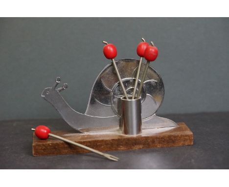 A Snail cocktail stick holder on wooden base with four cocktail forks. 