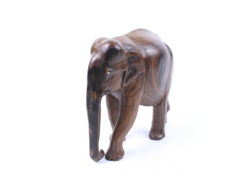 A 20th century hand carved Indian hardwood elephant figure. Striding, with trunk pendant. H26cm