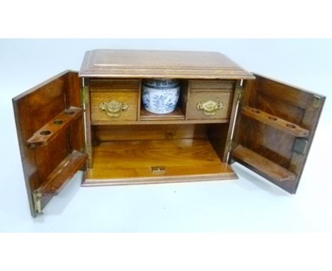 AN EDWARDIAN OAK SMOKER'S COMPANION BOX two decorative panel doors opening to reveal a fitted interior with pipe racks, drawe
