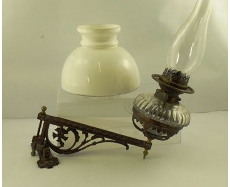 A LATE VICTORIAN WALL MOUNTING OIL LAMP, having a decorative cast iron arm supporting a clear glass reservoir with chimney an