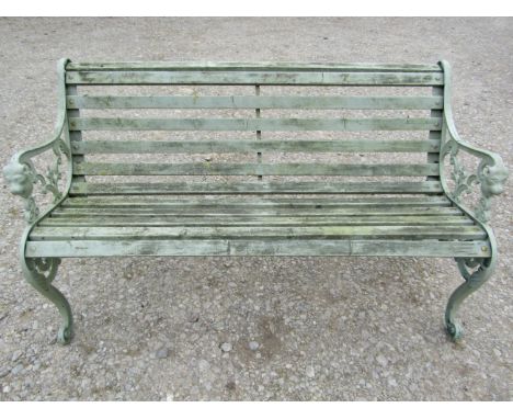 A light green painted garden bench with wooden slatted seat raised on decorative pierced and scrolled cast alloy end supports