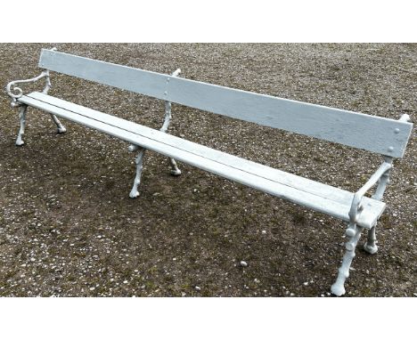 A long park/railway waiting bench with painted finish, wooden slatted seat and back rail raised on naturalistic cast iron twi