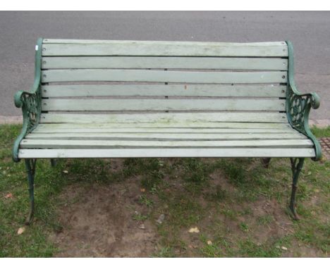 A two seat garden bench with painted wooden slatted seat raised on decorative pierced cast iron end supports with foliate and