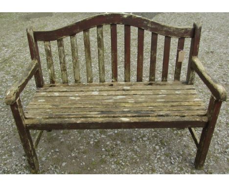 A weathered and stained teak garden bench with slatted seat and back beneath an arched rail, 120 cm, wide (af) 