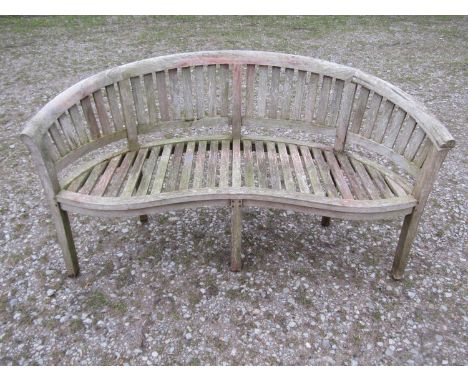 A weathered teak banana shaped garden bench, 156cm wide  (af) 