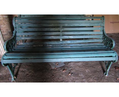 An old garden bench with painted wooden slatted seat and combined back raised on decorative cast iron armorial shield and vin