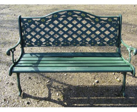 A green painted garden bench with wooden slatted seat beneath a cast iron pierced lattice panelled back with repeating foliat