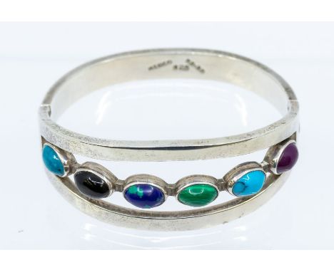 A silver and stone set hinged bangle, comprising six various oval cabochon stones set to the front, inset within an open silv