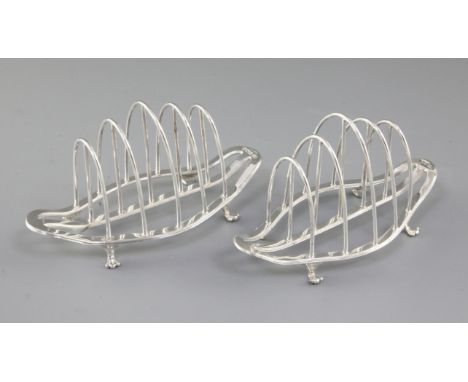 A matched pair of George V silver toast racks, by George Howson, hallmarked Sheffield 1922 and 1930, of boat shape, on four p