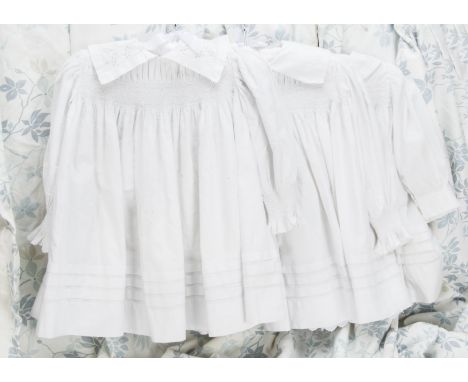 Three whitework children’s smocks, all smocked across the top, two at wrist, all with tucked skirts and mother of pearl butto