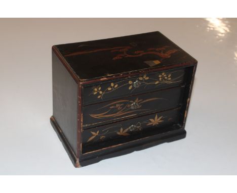 A lacquered three drawer chest and contents including Battersea enamel pill box, scent bottle, brooches etc.
