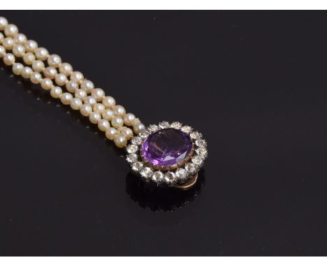 A graduated three row pearl necklace, with gold clasp, tests as 14ct or higher, set with a central amethyst surrounded by bla