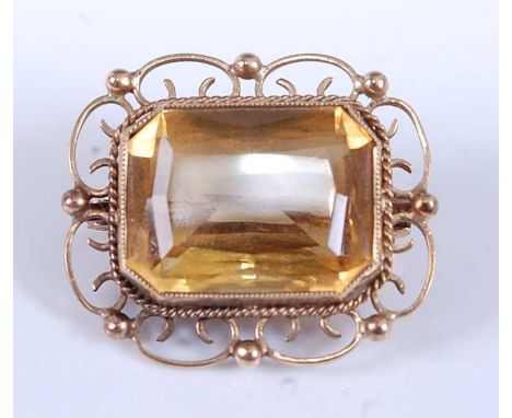 A yellow metal citrine brooch, featuring a step cut citrine bezel set within an open scrollwork mount, with roller catch fast