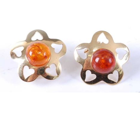 A pair of yellow metal amber stud earrings, each comprising a 9.85mm amber cabochon with a five petal mount with cut-out hear