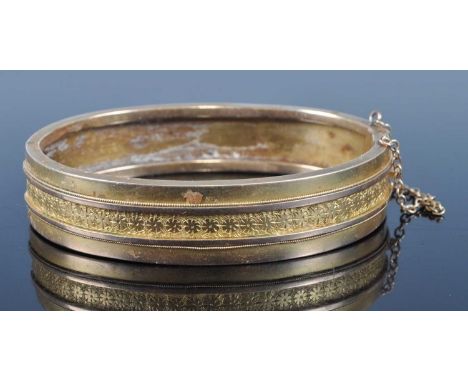 An early 20th century yellow metal hinged bangle, one half with raised tramline and engraved decoration, unmarked but tests a