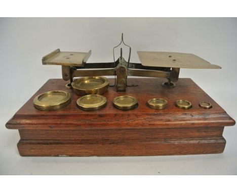 A 19th century set of postal scales with numeric stamped plate and seven graduated disk shaped weights upon a rectangular oak