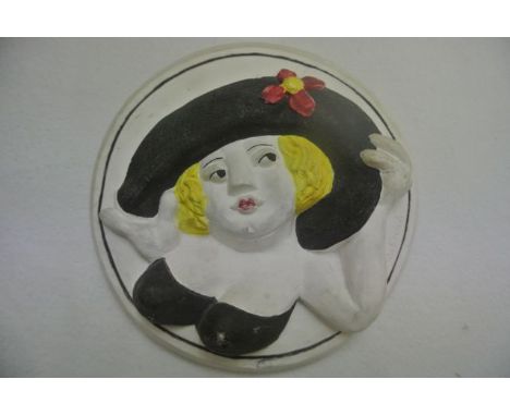 A relief moulded painted plaster panel of circular form showing a buxom lady in black hat, impressed signature B Cook for Ber