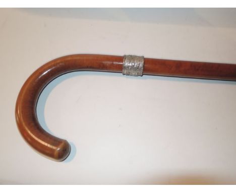 A polished Malacca walking stick with usual crooked handle above a white metal collar bearing embossed detail of Dutch childr