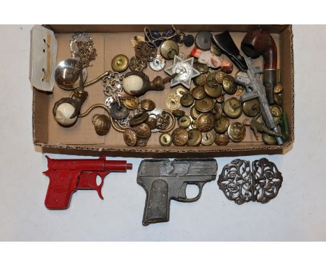 A box containing ornate white metal buckle, brass and other badges; toy guns; pipe etc.