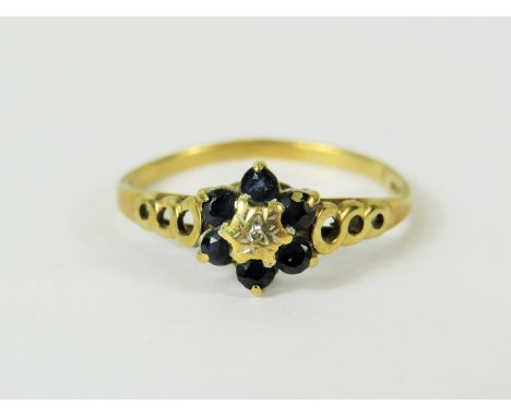 9ct Yellow Gold ring set with a small central Diamond and surrounded by  six small Sapphires.   Ringed shoulder decoration.. 