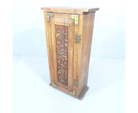 An Arts and crafts oak single door cabinet with brass mounts and applied carved foliate decoration. The single door revealing